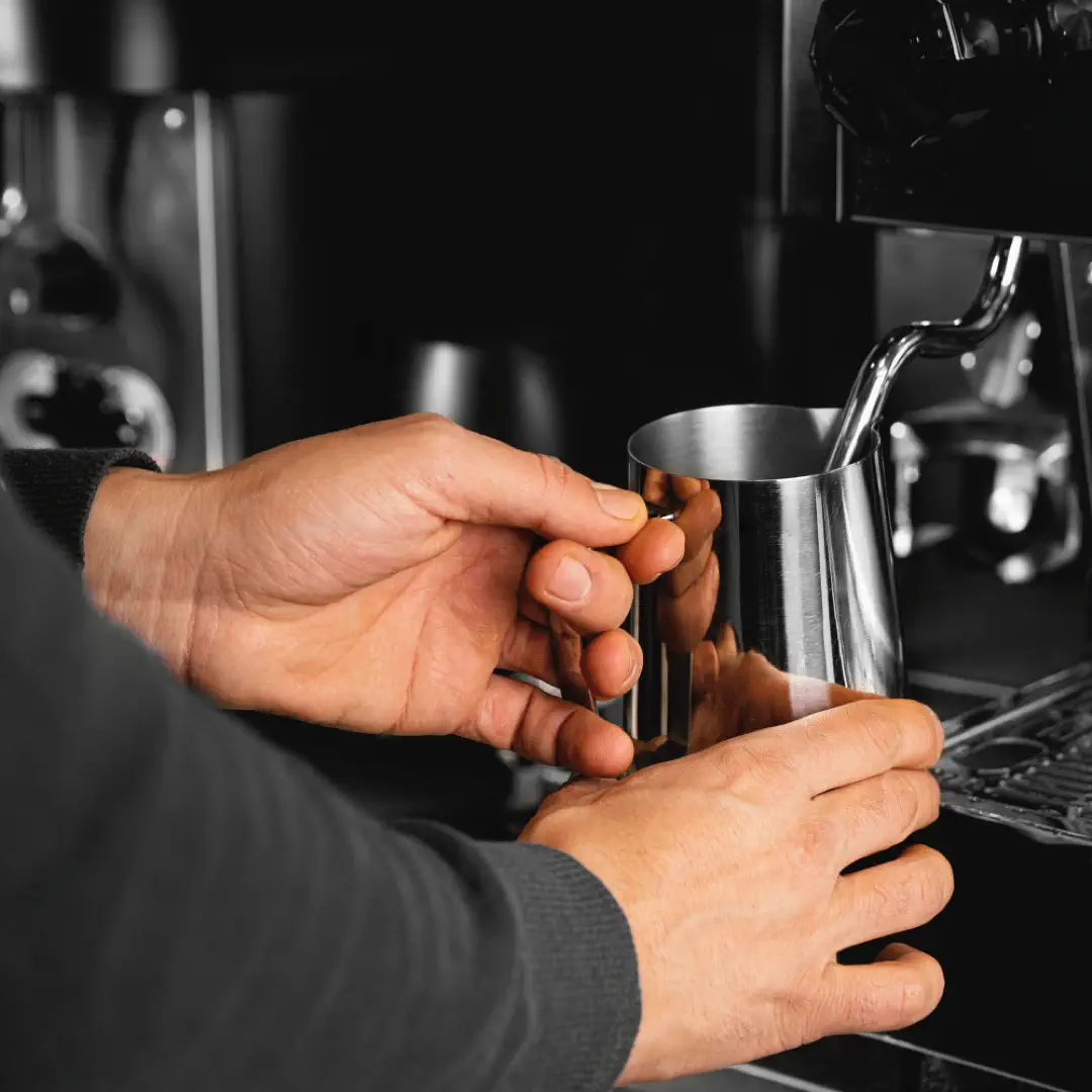 Barista schäumt Milch an einer Siebträgermaschine für die Zubereitung eines Kaffees auf